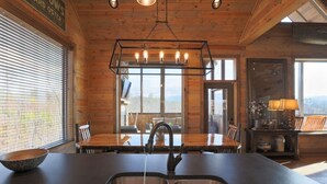 A wooden cabin interior with a large dining table, a modern kitchen with a double sink, and a hanging light fixture. - Renewed Spirit 7 Bedroom Cabin with Heated Pool (Sevierville)