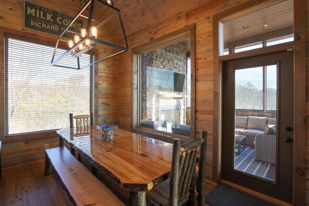 A wooden interior with a large dining table, benches, and a stone fireplace.