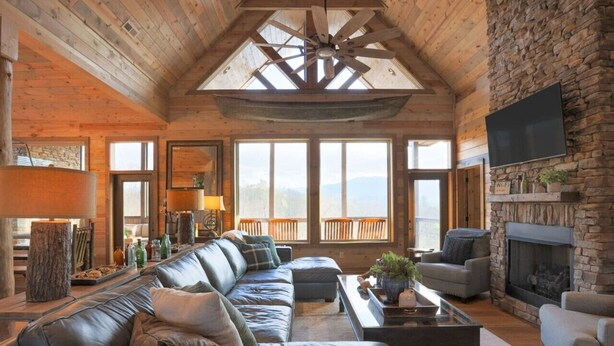 A spacious living room with a large leather sofa, a fireplace, and a stone wall. - Renewed Spirit 7 Bedroom Cabin with Heated Pool (Sevierville)