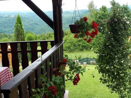 Un balcón de madera con macetas de geranios y vistas a un paisaje verde exuberante.