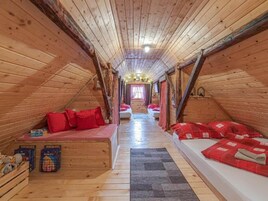 Un acogedor dormitorio en el ático con paredes de madera y techos inclinados, con dos camas con ropa de cama roja, una pequeña zona de estar y una ventana con cortinas.