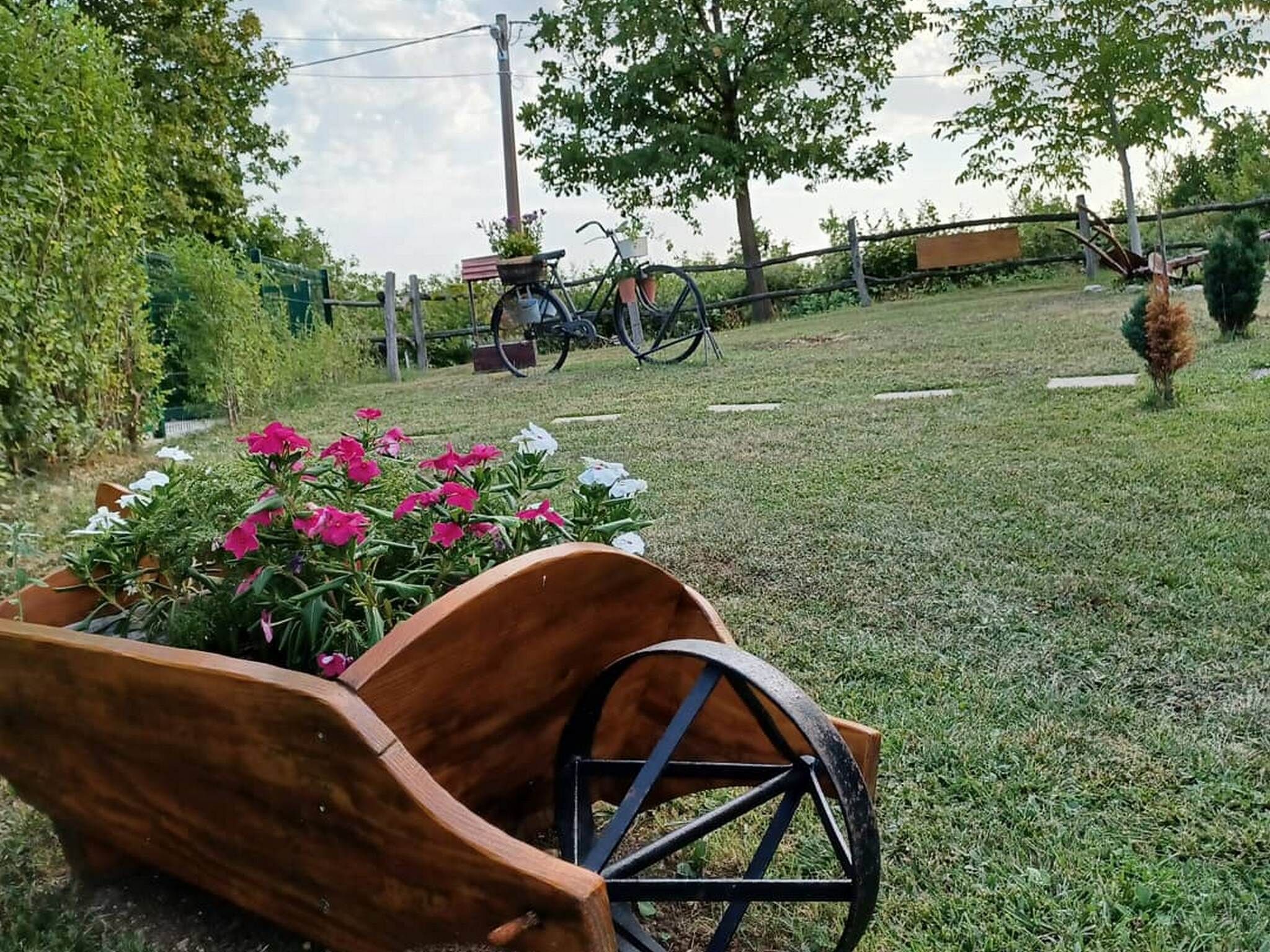 A wooden bench with a metal frame, a garden with pink and white flowers, and a bicycle in the background.