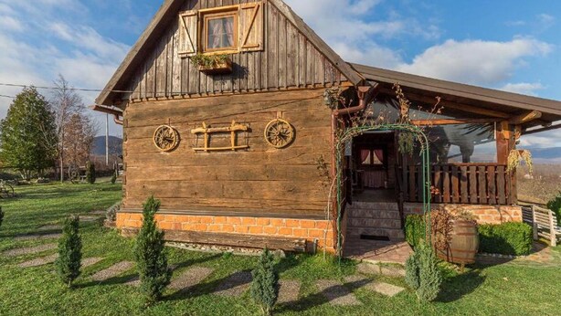 Une maison rustique en bois, dotée d’un toit à pente, d’un porche en bois surmonté d’une arche verte et de fondations en briques.