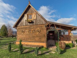 Una casa rústica de madera con techo inclinado, un porche de madera con un arco verde y cimientos de ladrillo.