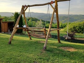 Un columpio de madera en un patio cubierto de césped, con vistas a colinas al fondo.