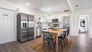 Una cocina moderna con armarios blancos, electrodomésticos de acero inoxidable y una mesa de comedor de madera con sillas.