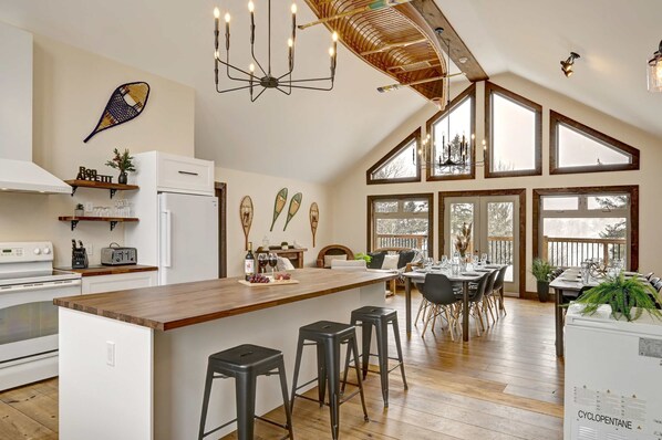 A spacious kitchen with a large island, bar stools, and a dining area with a high ceiling and large windows.