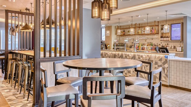 A modern bar area with a bar counter, stools, and hanging pendant lights. - Premier Inn London Canary Wharf - Westferry (London)