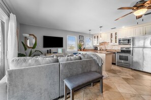 Relax in this spacious living area with a comfortable sofa and bench, featuring a well-equipped kitchen with a large island and sink.