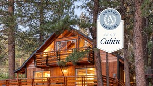 Una cabaña con balcón, ventanas amplias y un cartel que indica que es finalista al premio a la mejor cabaña.