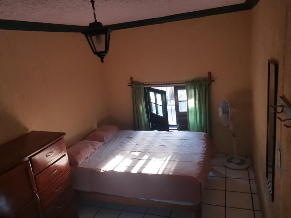 Un dormitorio con cama, cómoda, ventilador y ventana con cortinas.