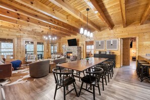 A spacious wooden cabin with a large dining table, multiple chairs, a fireplace, and a cozy seating area.