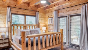 Una habitación de cabaña de madera con cama, ventilador de techo y ventanas amplias.