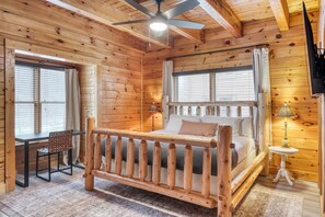 A wooden cabin room with a bed, a desk, and a chair.