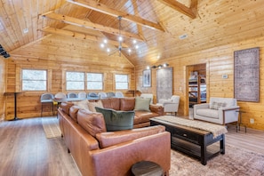 A spacious log cabin interior with a large leather sofa, a coffee table, and a dining area with chairs.