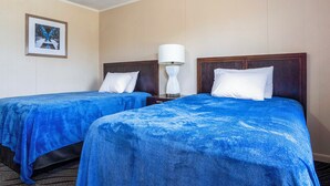 A hotel room with two beds, each with a blue bedspread and white pillows. There is a framed picture on the wall and a white lamp on a bedside table. - OYO Hotel Opp AL Floral Hwy (Opp)