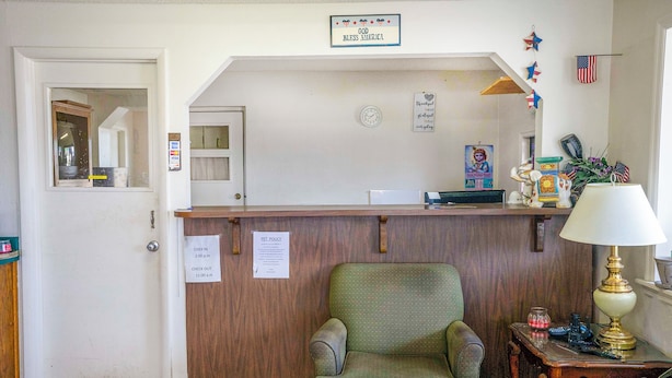 A reception area with a wooden desk, a green armchair, a lamp, and a sign indicating pet policy hours. - OYO Hotel Opp AL Floral Hwy (Opp)
