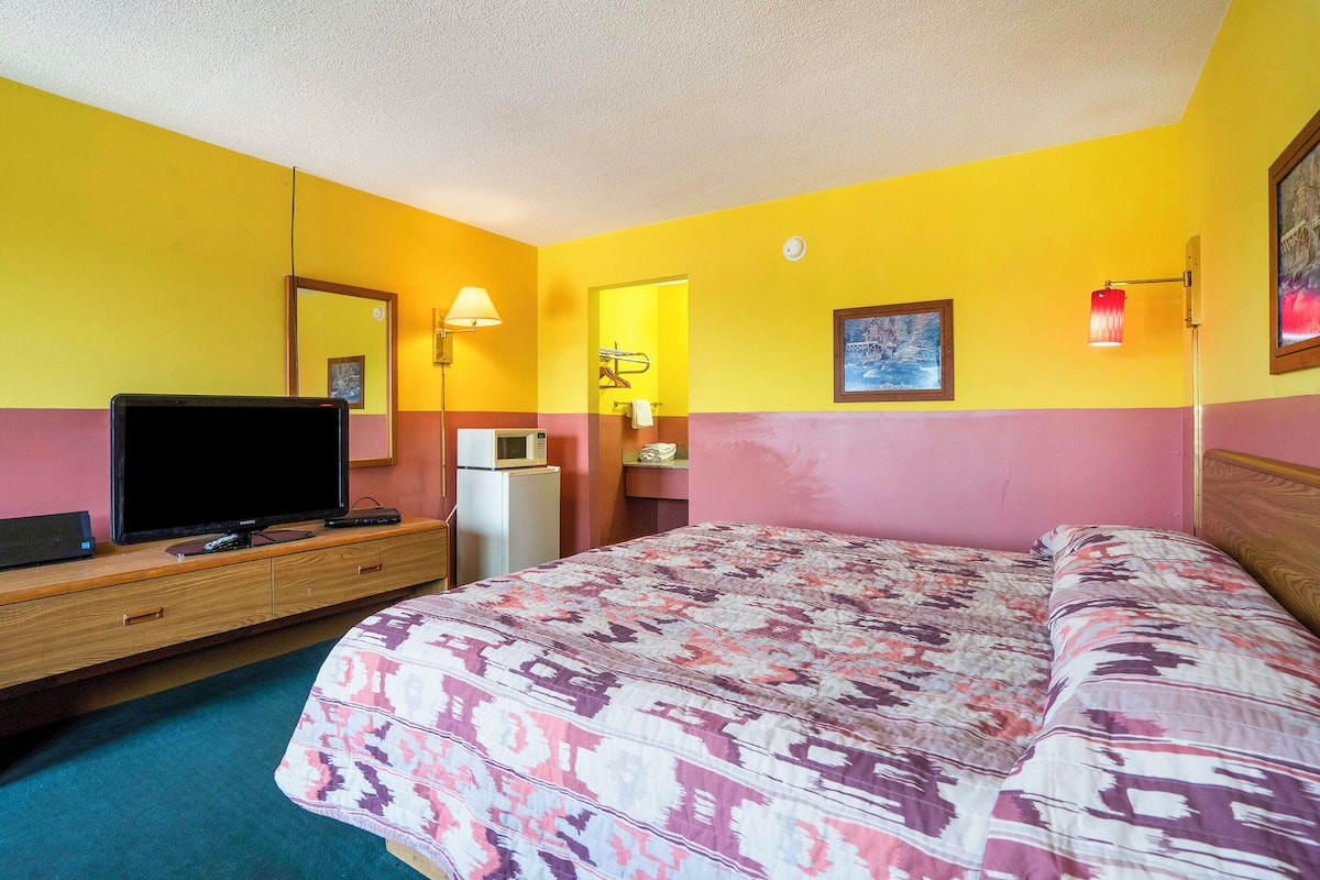 Habitación de hotel con cama, televisor, microondas, cómoda y espejo.