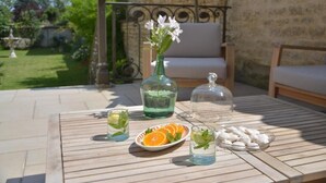 An outdoor patio with a wooden table set for a meal, featuring a plate of sliced oranges and mint leaves, a glass of water, and a bottle of water. - La Maison 19 (Niort)