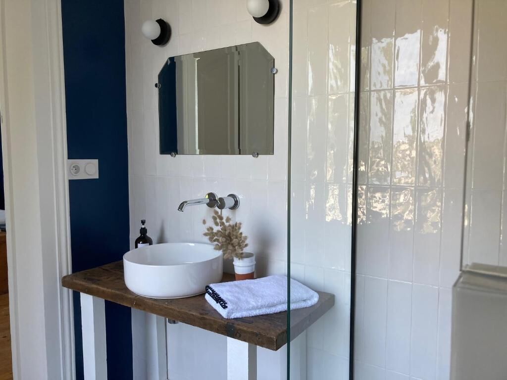 Une salle de bain avec un lavabo blanc, un plan de travail en bois, un miroir et une cabine de douche en verre.