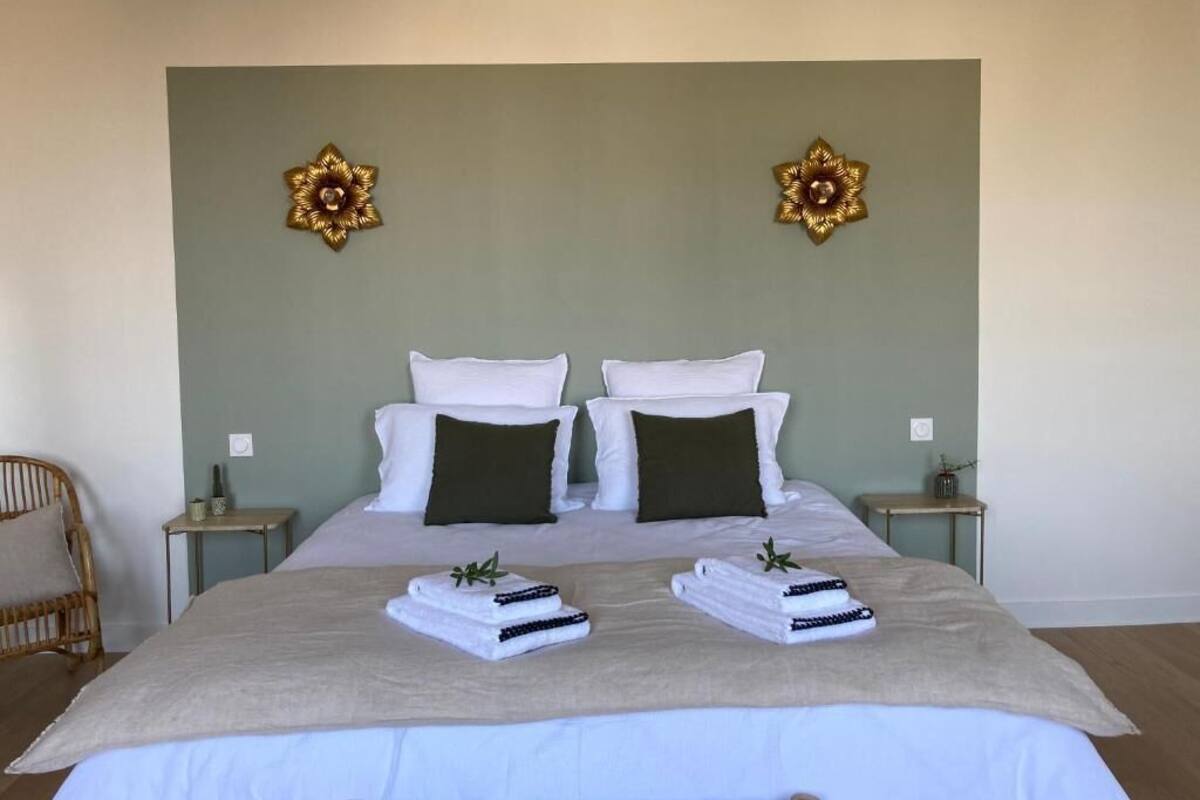 Una cama bien hecha con almohadas blancas y oscuras, dos mesitas de noche con lámparas y decoración en la pared.