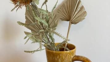 A brown ceramic mug with a handle, containing dried plants and a fan-shaped paper decoration.