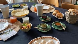 A dining table set with various dishes, including croissants, a bowl of fruit, and a plate of meringues. - La Maison 19 (Niort)