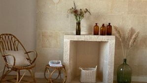 A room with a stone fireplace, wicker furniture, a white rug, and decorative bottles. - La Maison 19 (Niort)