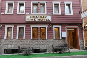 A building with a sign reading "Holiday Time Hotel." It features a stone facade, multiple windows, and outdoor seating with tables and chairs. - My Holiday Time Hotel (Istanbul)