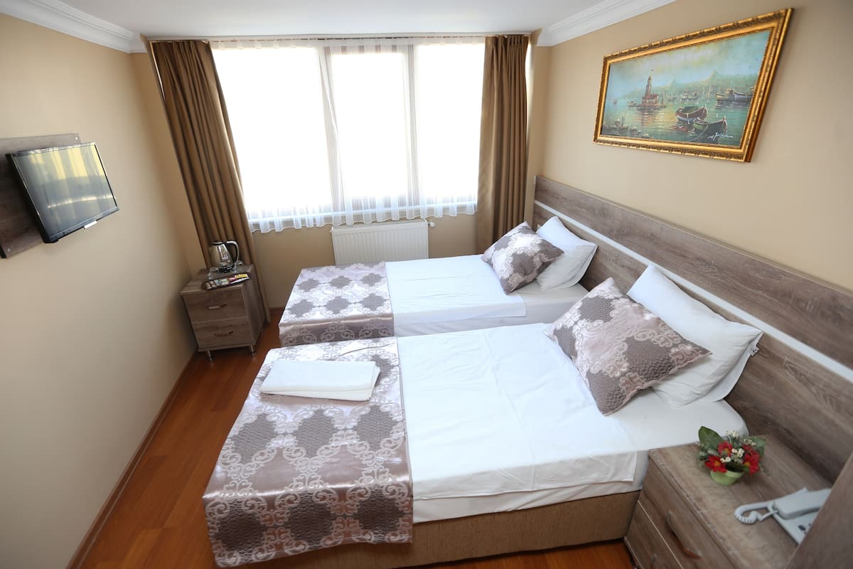 A hotel room with two beds, a television, a painting, and a window with curtains.