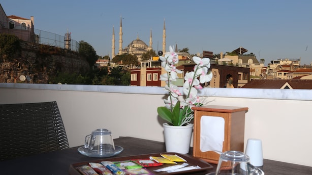 A table with snacks and a potted plant on a balcony overlooking a cityscape with a prominent mosque. - My Holiday Time Hotel (Istanbul)