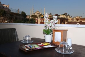 Une table avec des collations et une plante en pot sur un balcon donnant sur un paysage urbain, avec une mosquée imposante en évidence.