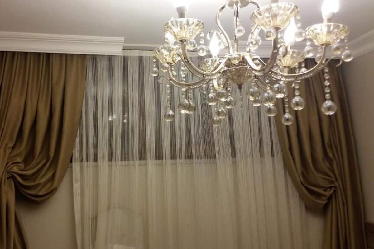 A room with a chandelier, draped curtains, and a sheer curtain.