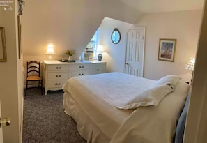A bedroom with a bed, dresser, chair, and a small desk with a lamp.