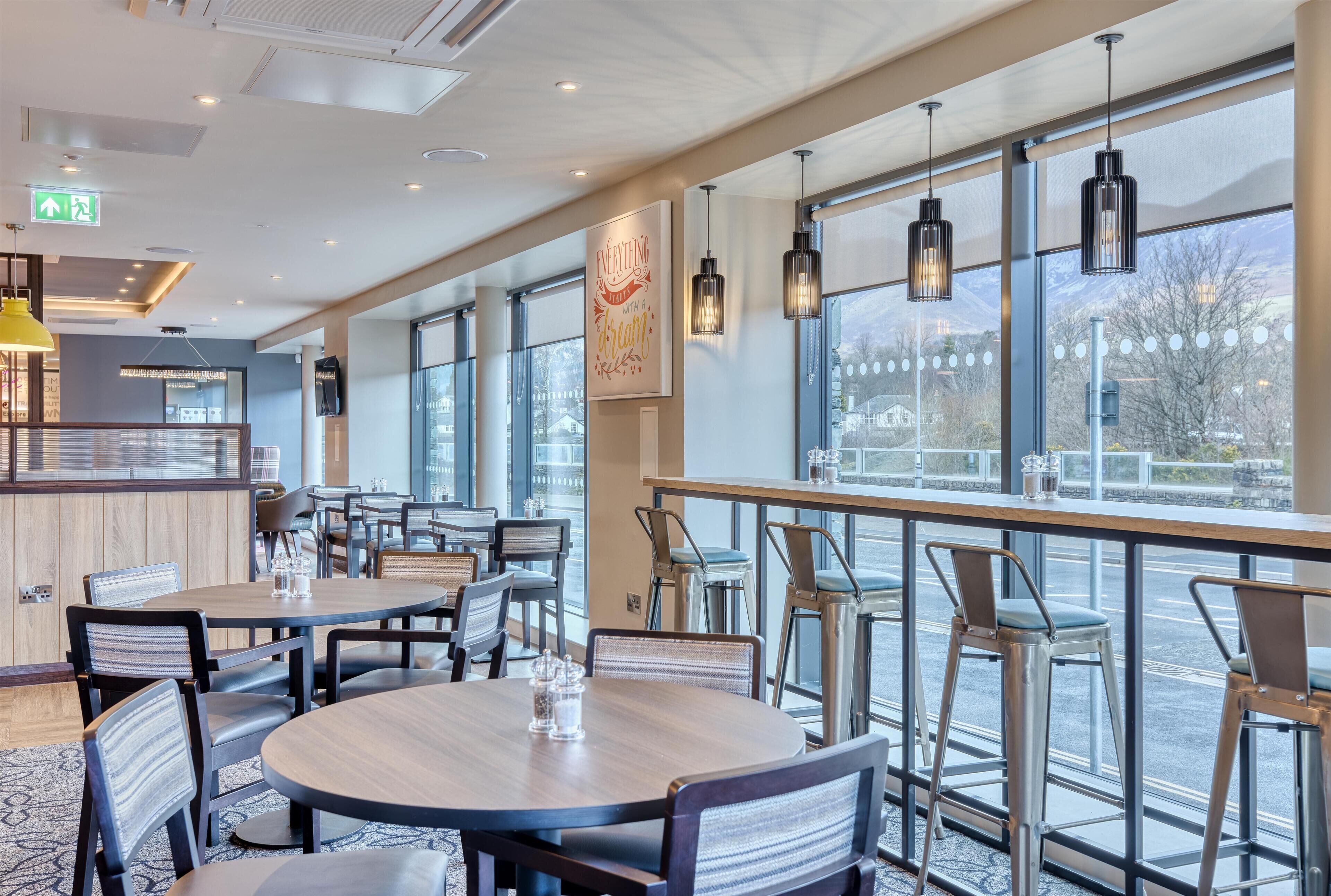 Een modern restaurant met ronde tafels, een bar en grote ramen met uitzicht.