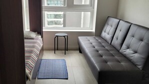 Ein kleines Zimmer mit Bett, Sofa, Tisch und Fenster mit Blick auf Gebäude.