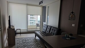 Ein modernes Wohnzimmer mit einer Couch, einem Esstisch und Blick auf einen Balkon mit einem Sessel.