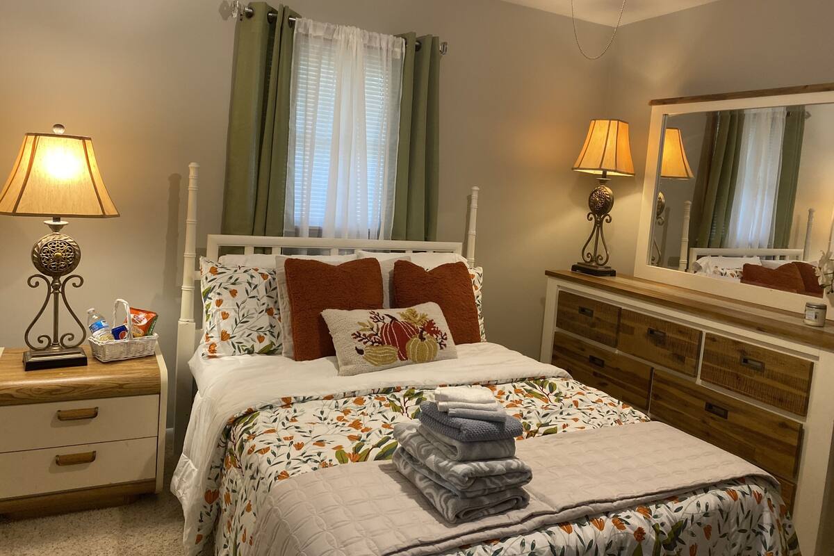 A neatly arranged bedroom with a bed, two bedside tables, a dresser, and a mirror.
