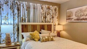 Ein Schlafzimmer mit einem Bett, floralen Vorhängen, zwei Nachttischlampen und einem Bild an der Wand.