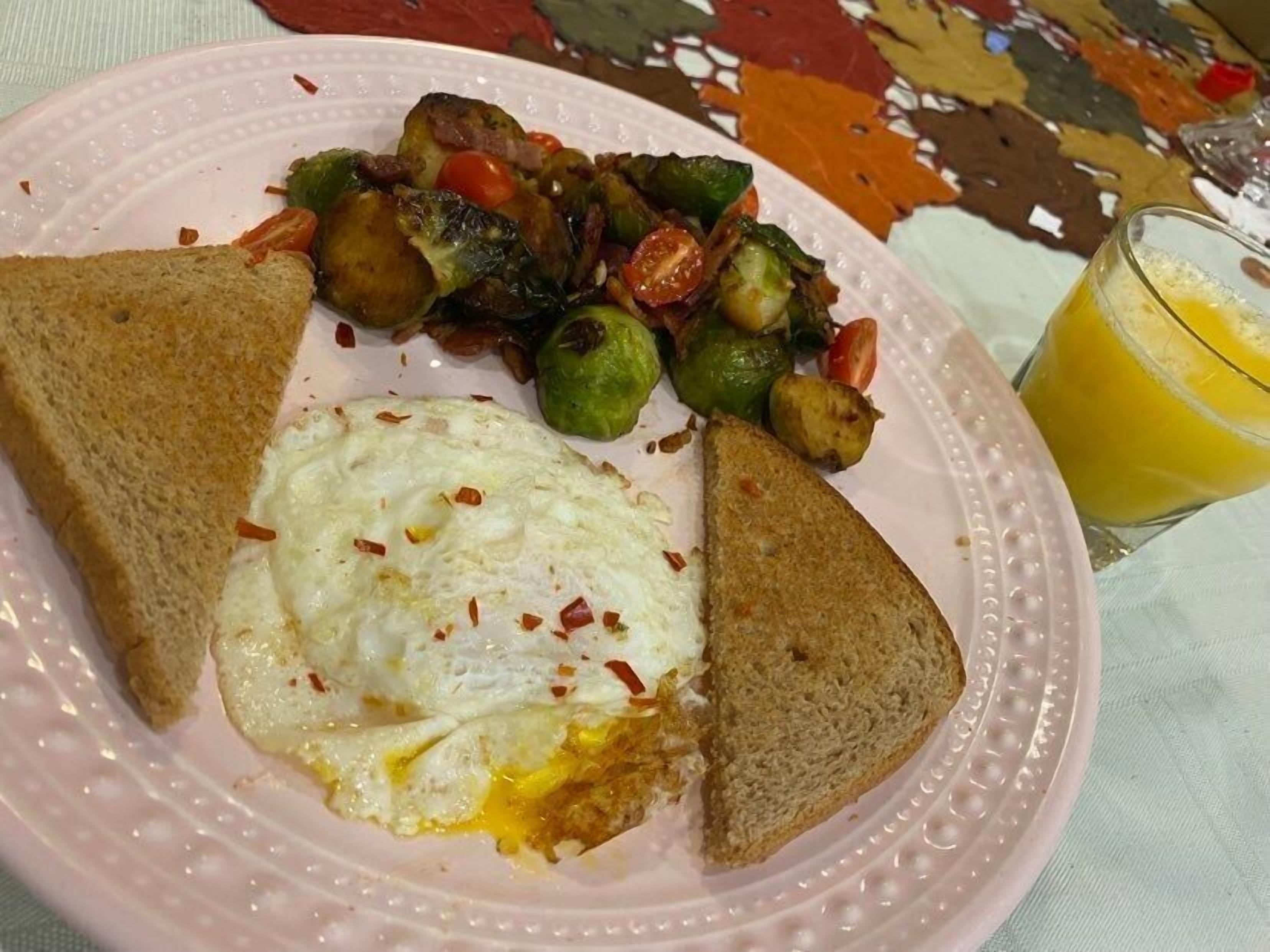 Une assiette contenant des œufs brouillés, des légumes rôtis et des toasts, accompagnée d’un verre de jus d’orange.