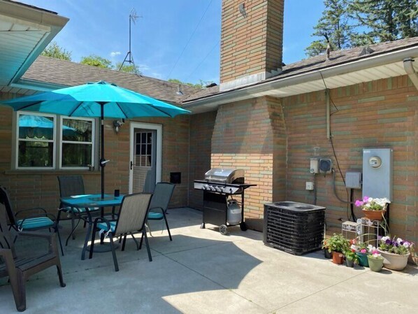 A patio with a grill, chairs, and a table under a blue umbrella. - The Sanctuary On Huron River (Flat Rock)
