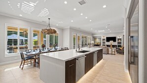 A modern kitchen with a large island, built-in appliances, and a dining area with a view of the outdoors. - The Rose at Montage - Ultimate Estate (Indio)