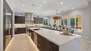 A modern kitchen with a large island, built-in appliances, and a dining area with a view of greenery. - The Rose at Montage - Ultimate Estate (Indio)