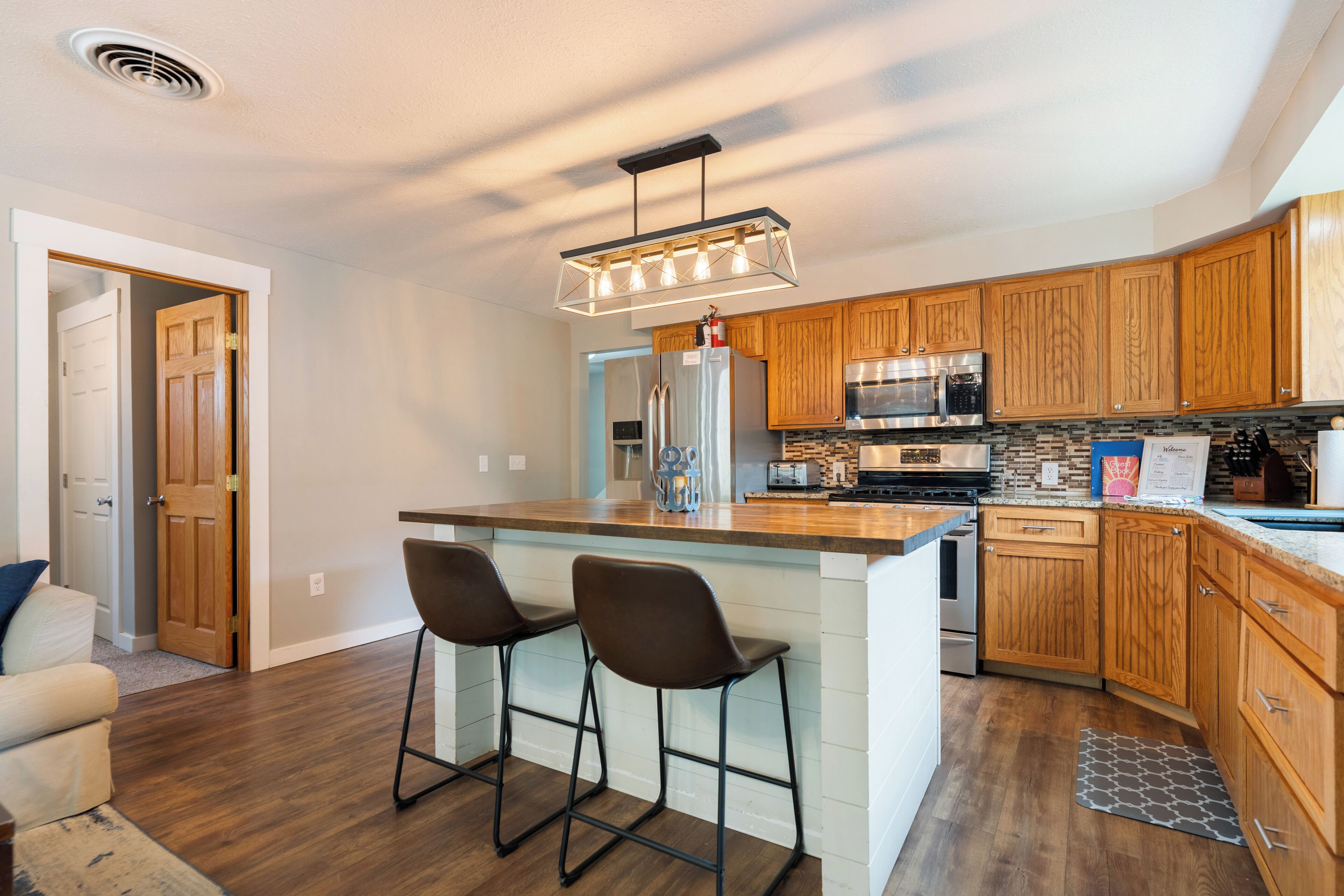 A modern kitchen with wooden cabinets, stainless steel appliances, and a bar stool seating area.