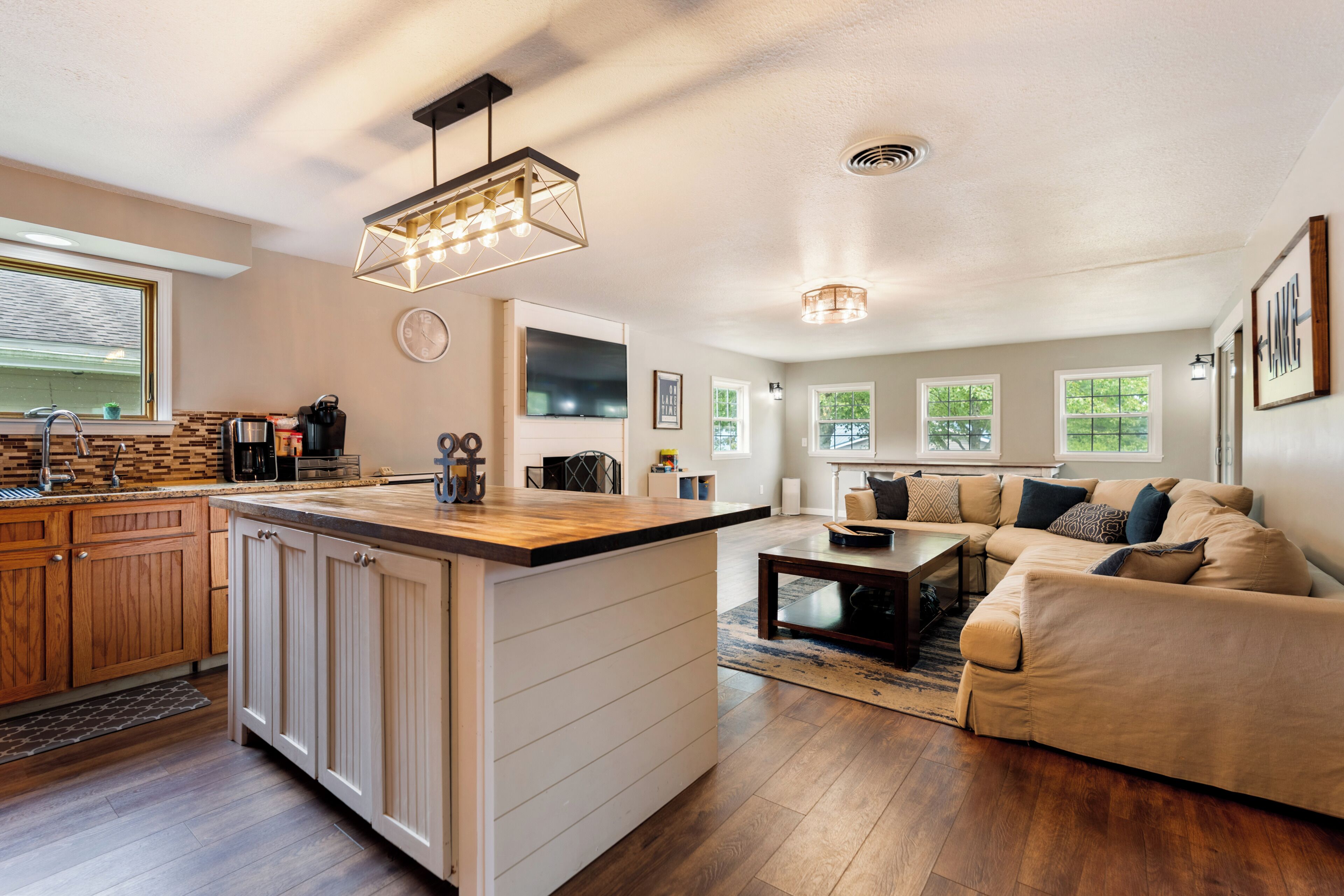 A modern kitchen with a central island, a dining area with a sofa, and a living room with a large window.