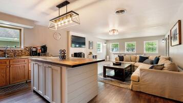 A modern kitchen with a central island, a dining area with a sofa, and a living room with a large window.