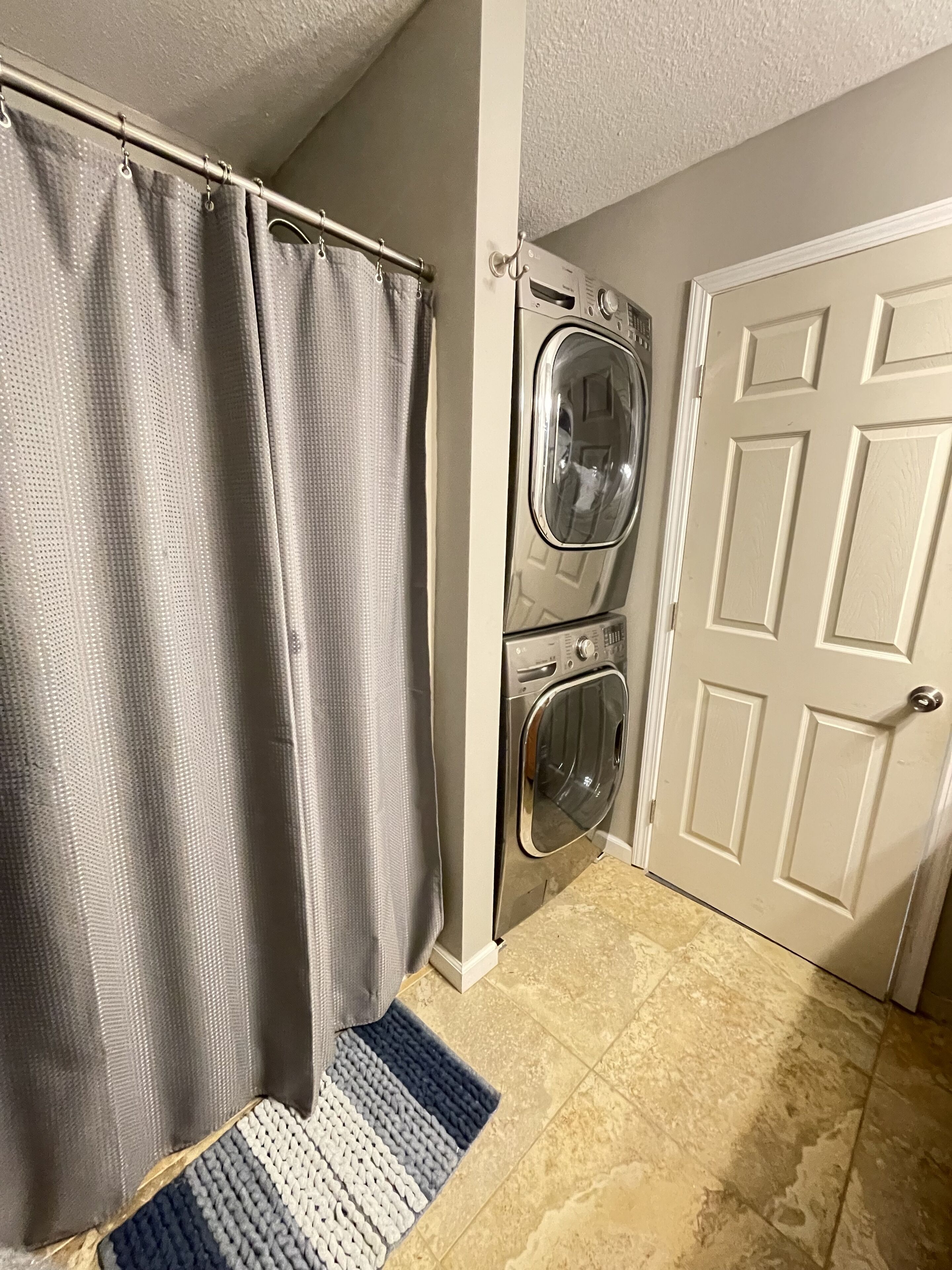 A laundry room with a washing machine and dryer, a shower curtain, and a door.