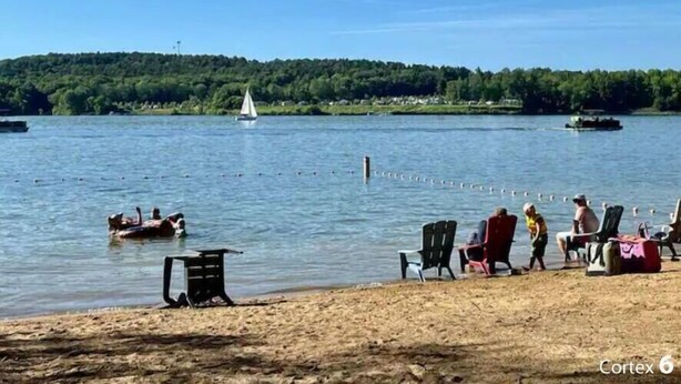 Escena junto al lago con barcos, sillas y una playa de arena.