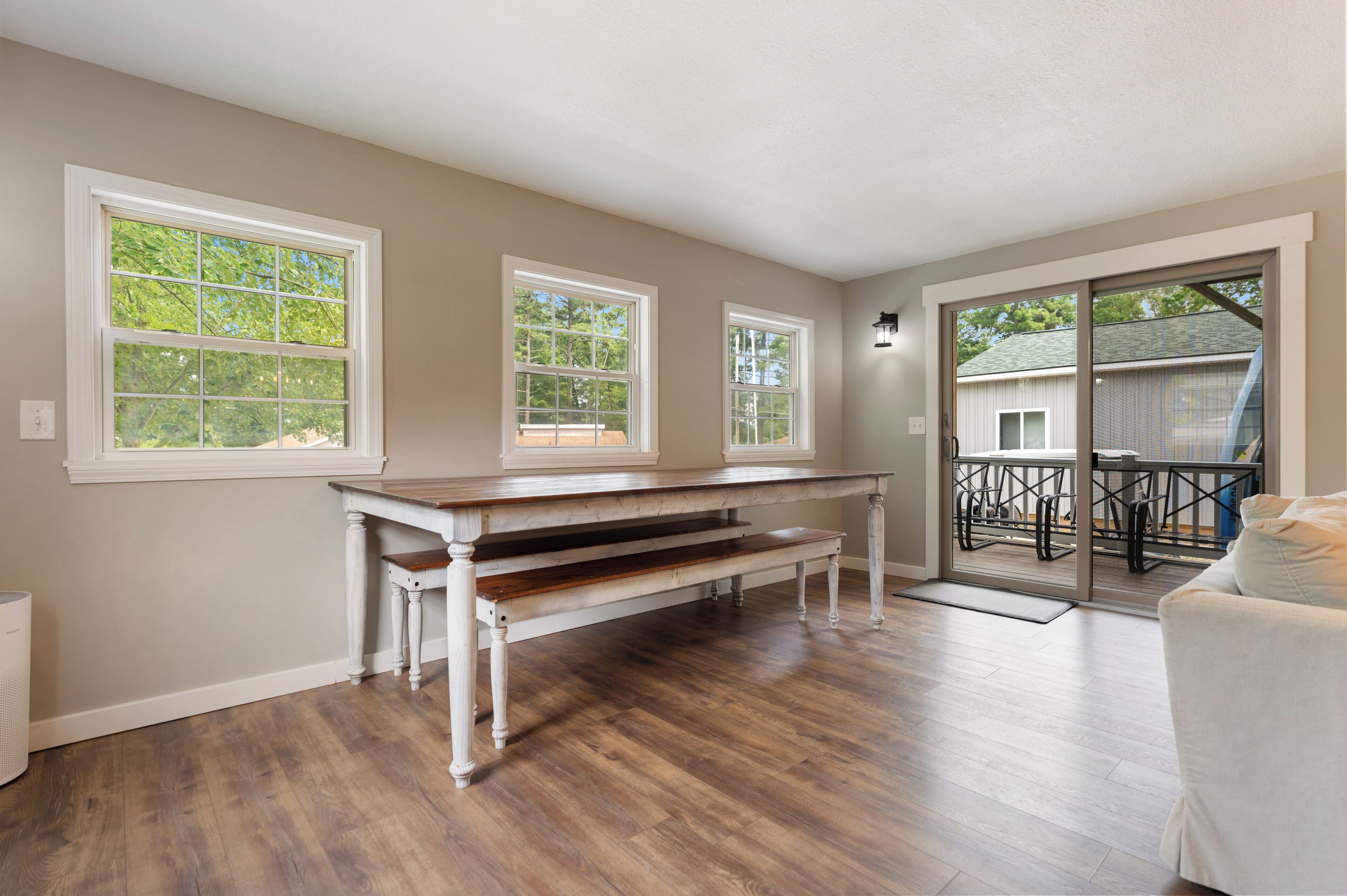 A spacious room with hardwood flooring, a white bench, and large windows offering views of trees.