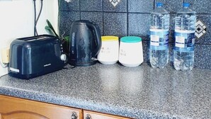 Uma cozinha com armários de madeira, bancada de granito, torradeira, chaleira, duas canecas e duas garrafas de água.
